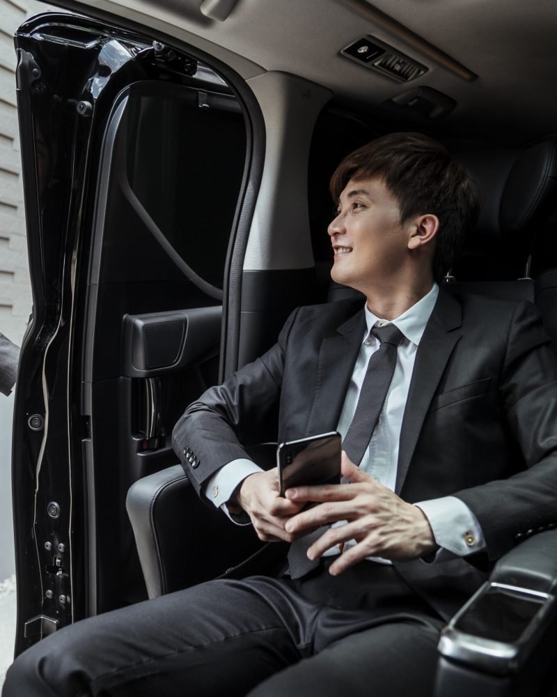 Asian businessman arriving at destination, chauffeur opening car door.